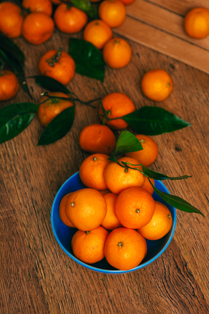 many fresh mandarin oranges in  blue bowl, standing on a wooden  tableの写真素材