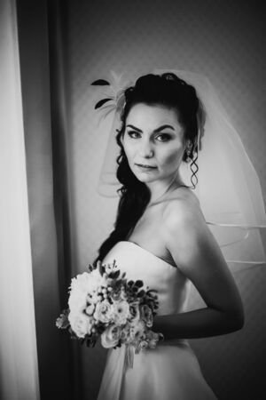 Black white photography beautiful young happy bride standing near the windowの写真素材