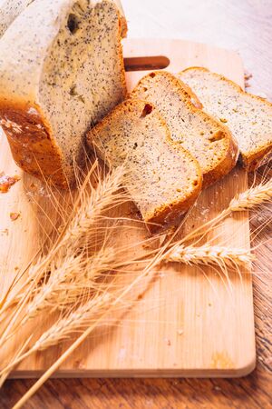 Close slice of fresh  bread with poppy seeds and wheat ears on wooden backgroundの写真素材
