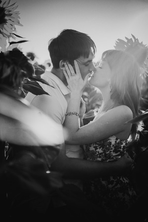 Black white photography romantic couple standing  and kissing on background summer meadow sunflower  sunsetの写真素材
