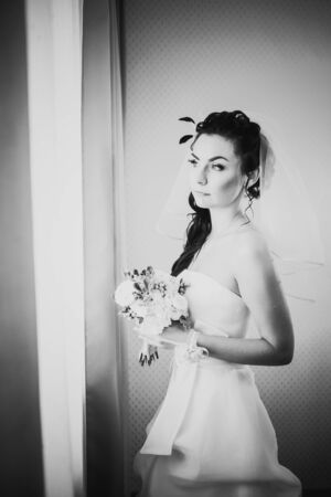 Black white photography beautiful young happy bride standing near the windowの写真素材