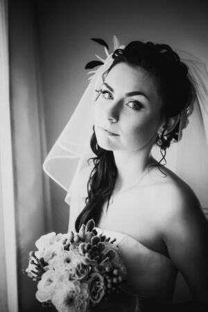 Black white photography beautiful young happy bride standing near the windowの写真素材