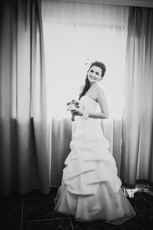 Black white photography beautiful young happy bride standing near the windowの写真素材