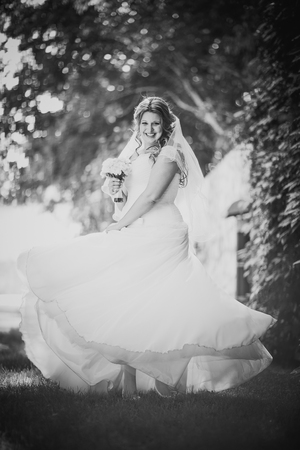 Black white   photography stylish beautiful happy bride holding  bouquet of flowers on a background of trees in the summer park full lengthの写真素材