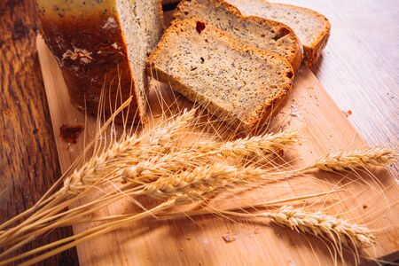 Close slice of fresh  bread with poppy seeds and wheat ears on wooden backgroundの写真素材