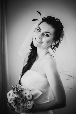 Black white photography beautiful young happy bride standing near the windowの写真素材