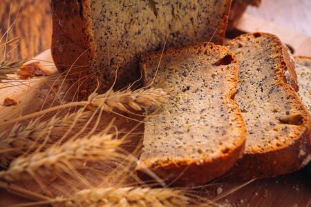 Close slice of fresh  bread with poppy seeds and wheat ears on wooden backgroundの写真素材