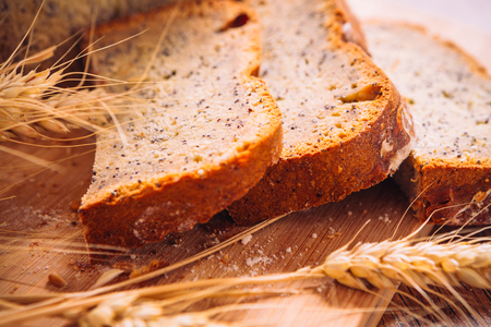 Close slice of fresh  bread with poppy seeds and wheat ears on wooden backgroundの写真素材