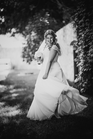 Black white   photography stylish beautiful happy bride holding  bouquet of flowers on a background of trees in the summer park full lengthの写真素材