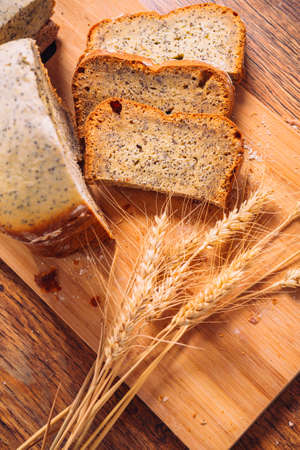 Close slice of fresh  bread with poppy seeds and wheat ears on wooden backgroundの写真素材