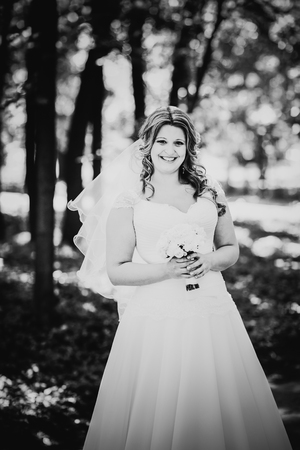 Black white photography stylish beautiful happy bride holding   bouquet of  flowers on a background of trees in the summer park close-upの写真素材