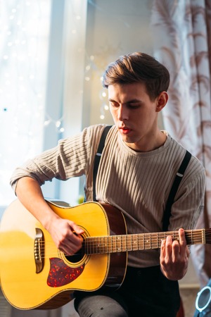 Young man sitting at home and playing  guitar dramaticの写真素材