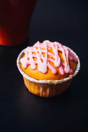 cupcake with pink frosting  and red cup on a wooden backgroundの写真素材