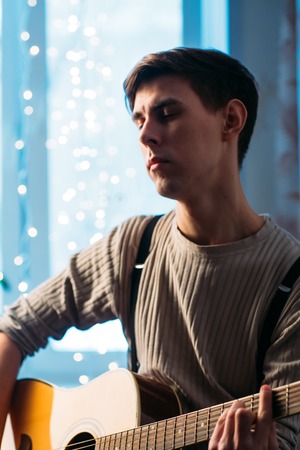 Young man sitting at home and playing  guitar dramaticの写真素材