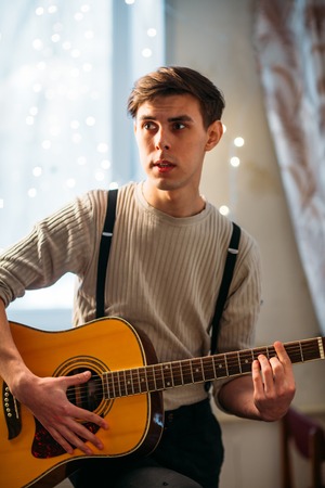 Young man sitting at home and playing  guitar dramaticの写真素材