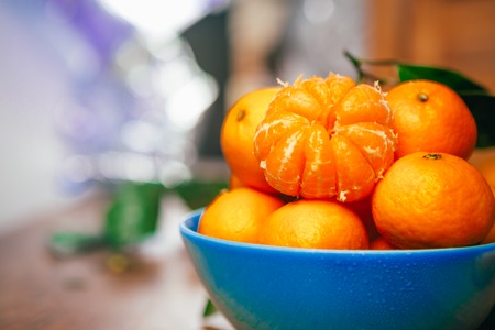 many fresh mandarin oranges in  blue bowl, standing on a wooden  tableの写真素材