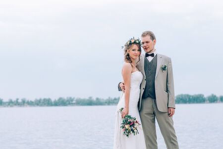 young groom and bride standing and hugging on the background of the river.の写真素材