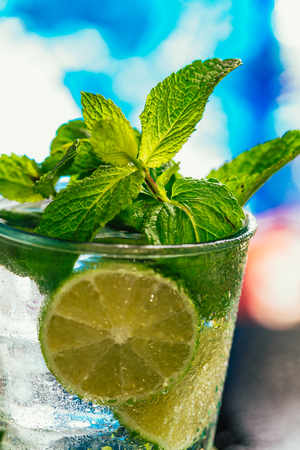 glass of mojito with lime and mint ice cube close-up with red straw on blue background.の写真素材