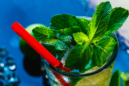 glass of mojito with lime and mint ice cube close-up with red straw on blue background.の写真素材