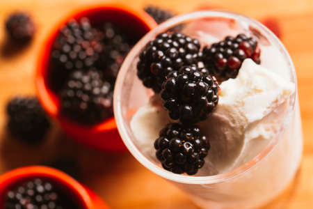 Blackberry ice cream in a cup and a glass on a background of wooden boards and a blurred green.
