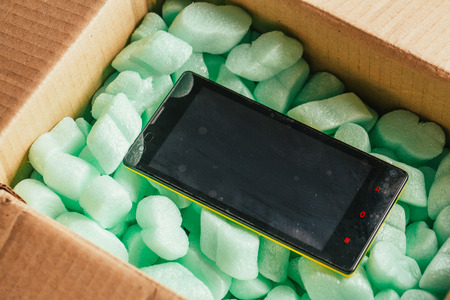 parcel of online shop, phone in a cardboard box on a green polystyrene.の写真素材