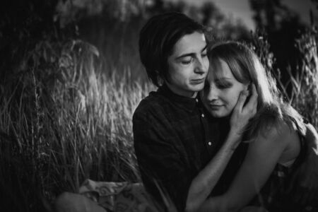 black and white guy and the girl sitting in the grass on a sunset background.