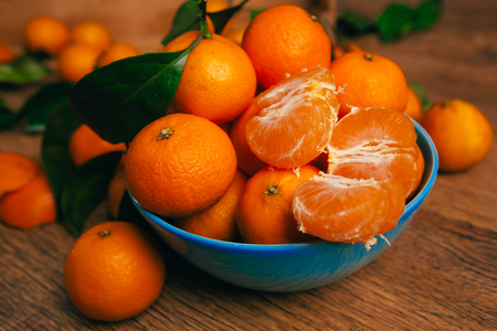 many fresh mandarin oranges in  blue bowl, standing on a wooden  table の写真素材