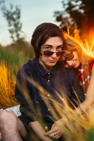 guy and the girl sitting in the grass on a sunset backgroundの写真素材