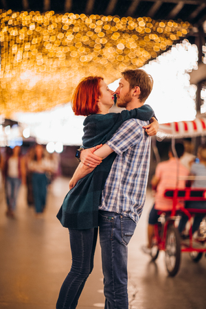 Happy couple embracing and kissing in the evening on a light garlandsの写真素材