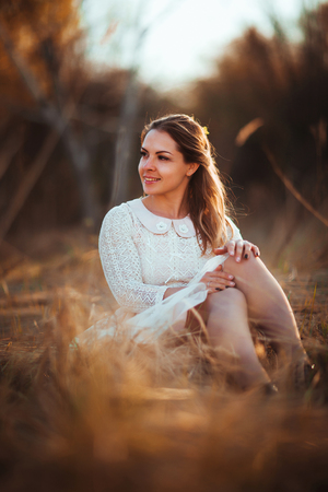 girl is sitting in the field on the sunset background.の写真素材