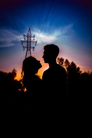 Silhouettes of a guy and girl in a field on a sunset background.の写真素材