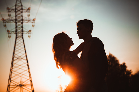 Silhouettes of a guy and girl in a field on a sunset background.の写真素材