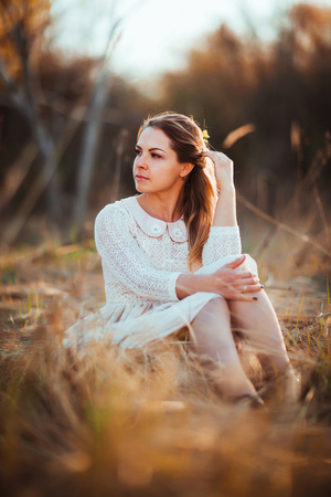 girl is sitting in the field on the sunset background.の写真素材