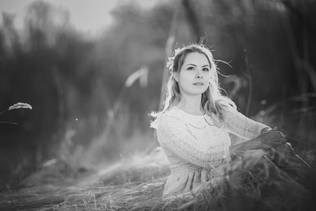 Blackwhite photo girl is sitting in the field on the sunset background.の写真素材