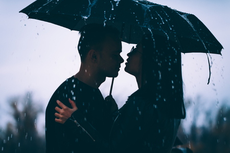 young couple standing under a dark umbrella.の写真素材