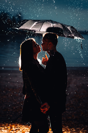 young man and woman under an umbrella and rain.