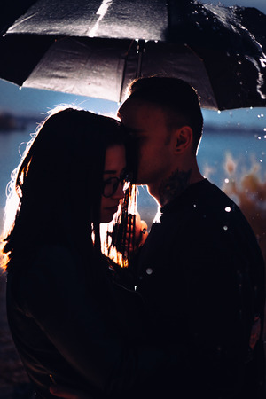 young man and woman under an umbrella and rain.の写真素材