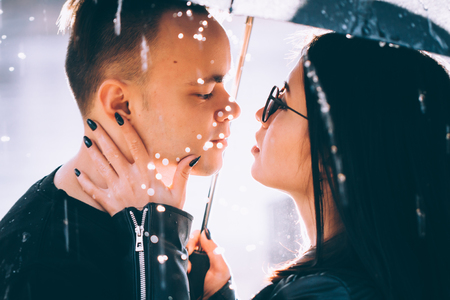 young couple standing under a dark umbrella.の写真素材