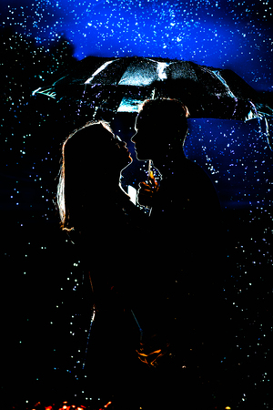 young man and woman under an umbrella and rain.の写真素材
