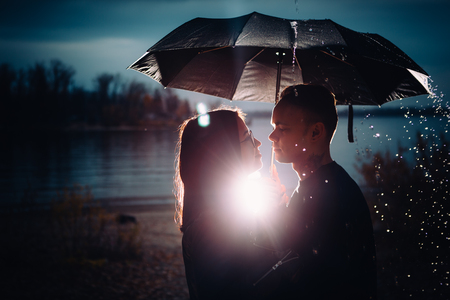 young man and woman under an umbrella and rain.の写真素材