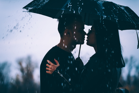 young couple standing under a dark umbrella.の写真素材