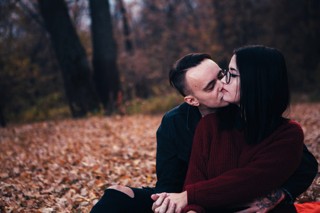young man and young woman are sitting on a plaid in an autumn forest.の写真素材