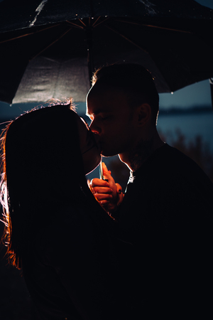 young man and woman under an umbrella and rain.の写真素材