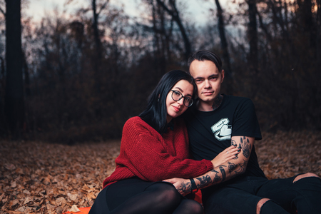 young man and young woman are sitting on a plaid in an autumn forest.の写真素材
