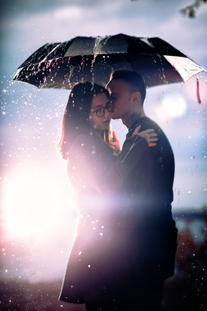 young man and woman under an umbrella and rain.の写真素材