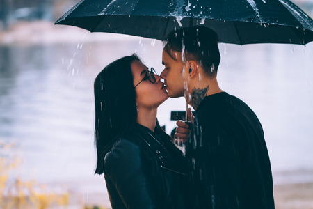 young man and woman under an umbrella and rain.の写真素材