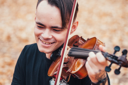 young man playing violin in the autumn forest.の写真素材