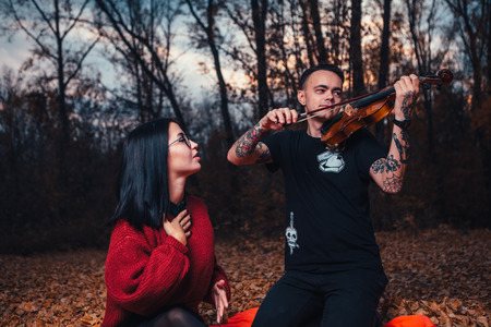 young man and young woman are sitting on a plaid in an autumn forest.の写真素材