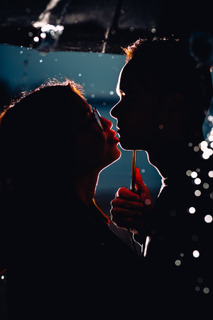 young man and woman under an umbrella and rain.の写真素材