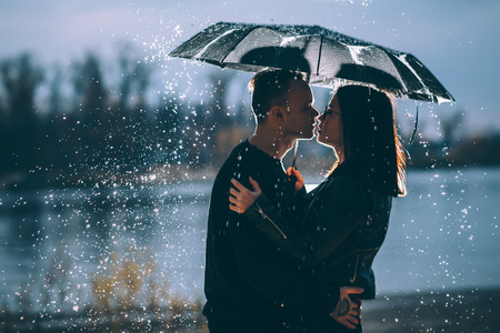 young couple standing under a dark umbrella.の写真素材